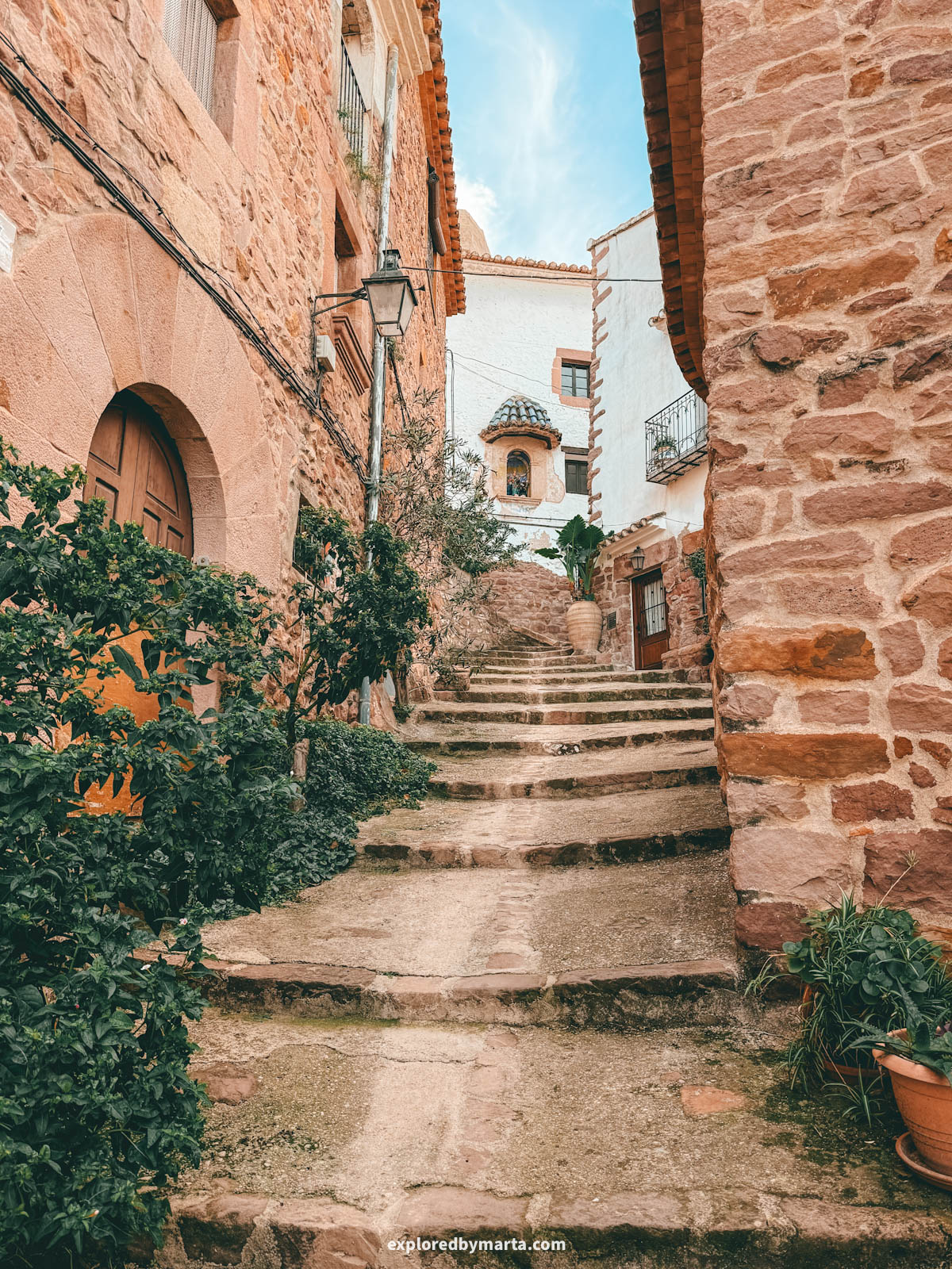 Narrow stone street lined with rustic houses and greenery in Vilafamés, Valencia Region, Spain