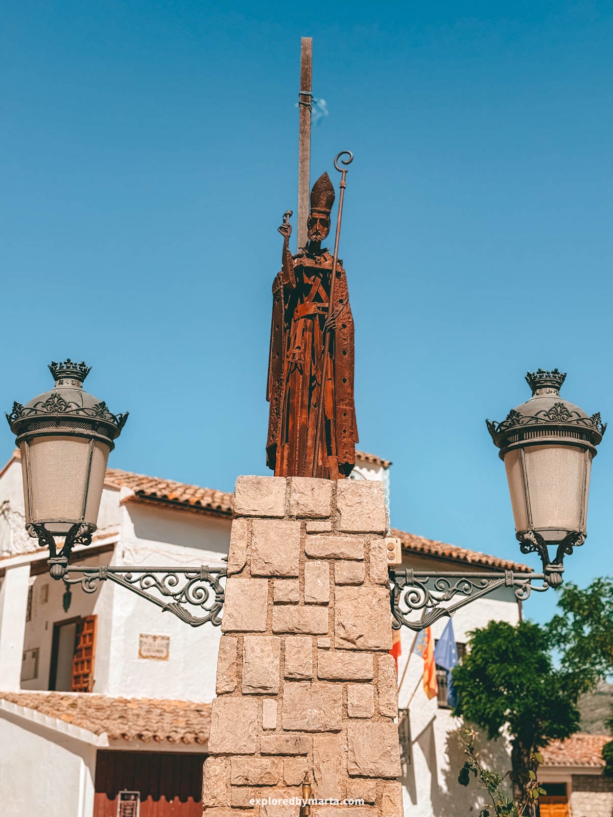 Metal statue of San Gregorio between the lamp posts at Plaza de San Gregorio in Guadalest, Spain