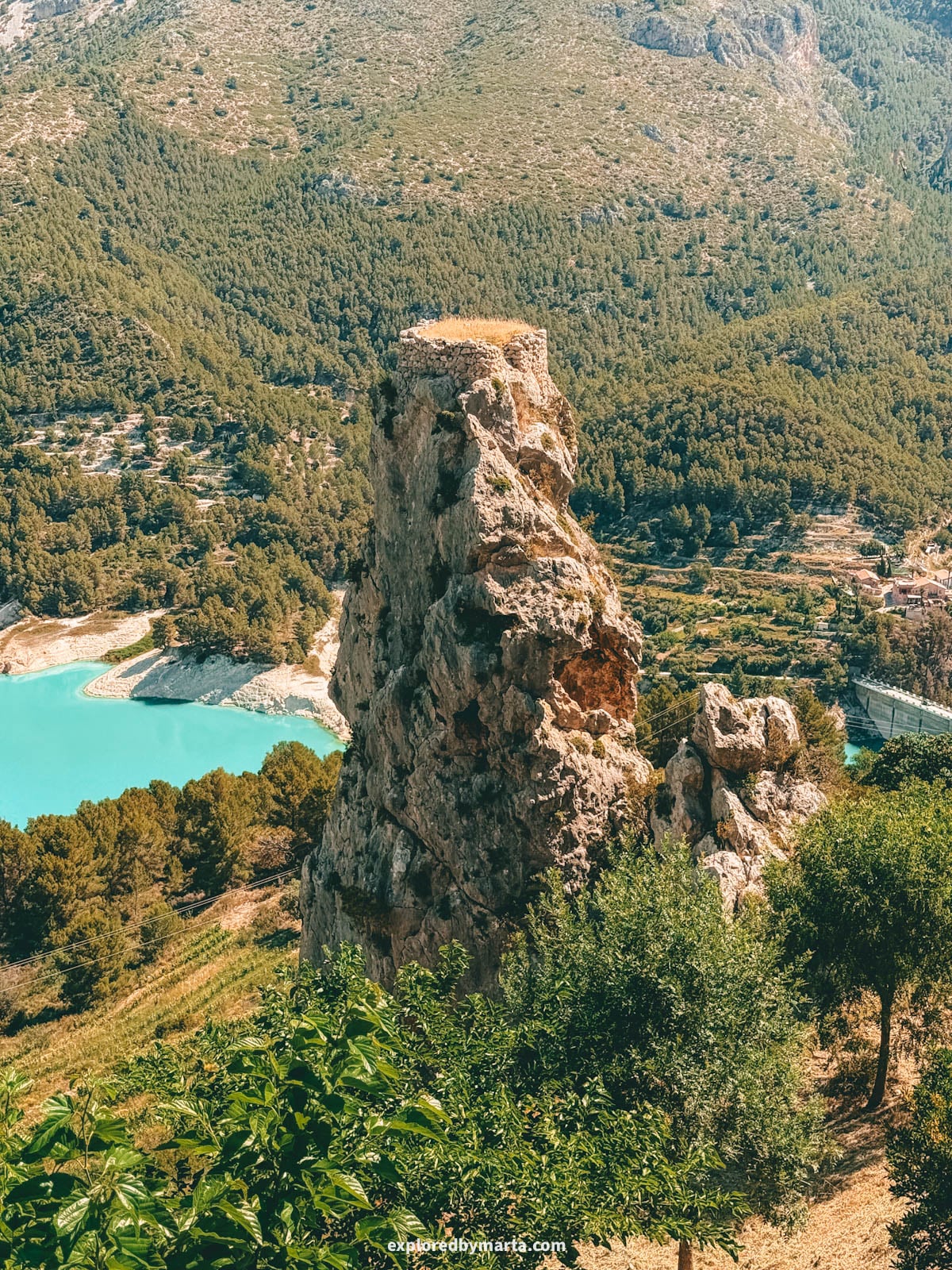 Torre de la Penya d'Alcalà on its rock with the reservoir seen from Plaza de San Gregorio in Guadalest, Spain