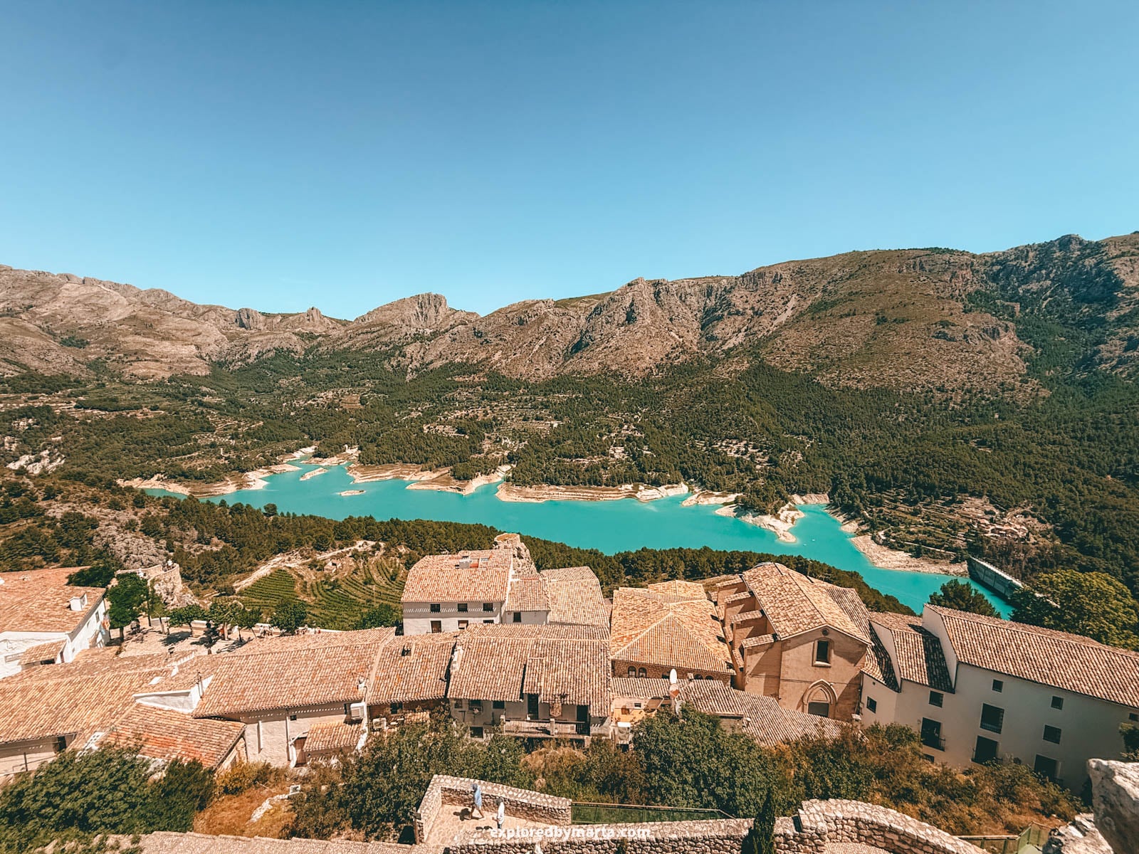 Turquoise Guadalest reservoir seen from the Castillo de San José castle over the village rooftops in Guadalest, Spain