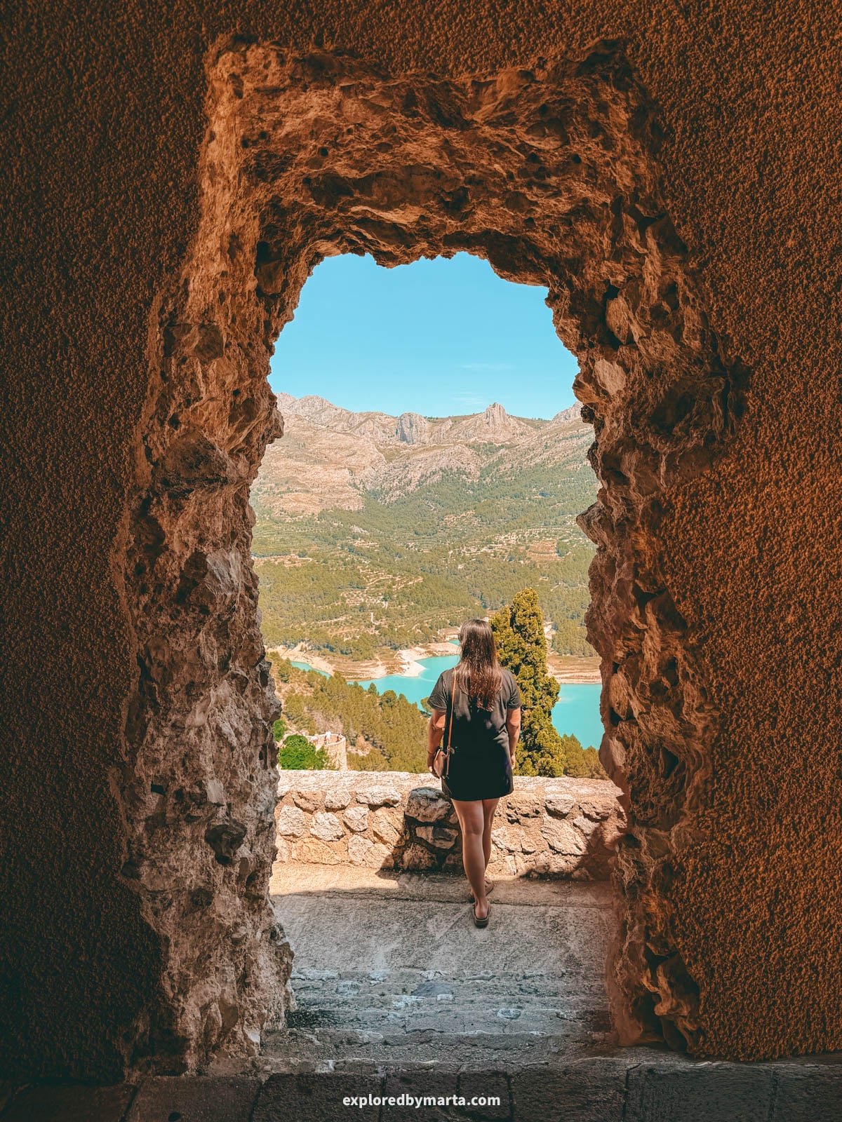 View of the Guadalest reservoir framed through the rock archway at San Jose Castle in Guadalest, Spain